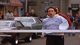 GIF of Jerry Seinfeld throwing his arms up as he runs through the finish line of a race